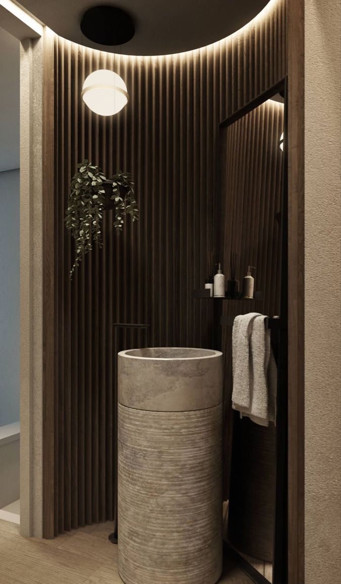 Modern luxury bathroom with a light concrete cylindrical pedestal sink, a matte black freestanding faucet, dark wood slatted accent walls with hidden lighting, and a spherical wall sconce.
