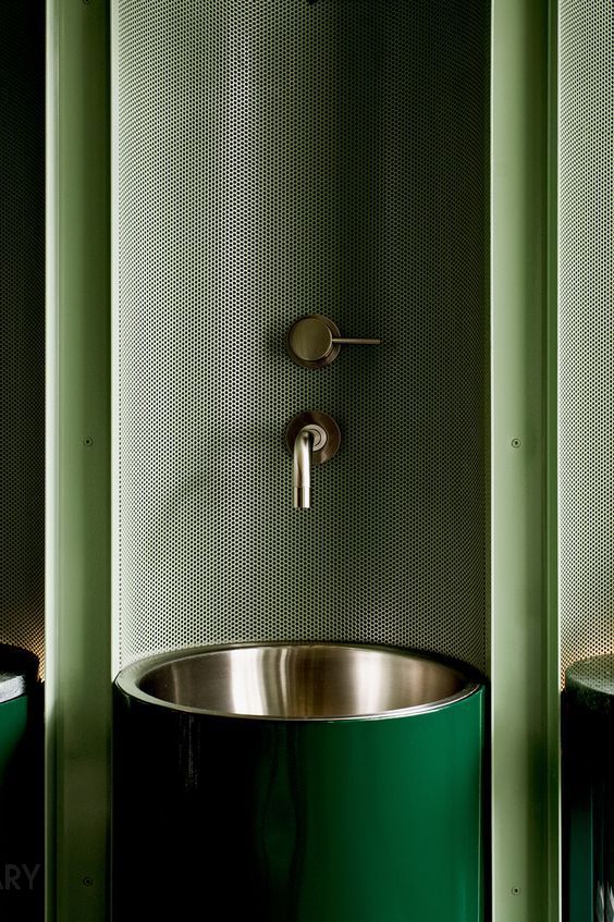 A custom deep green high-gloss pedestal sink with a stainless steel basin and wall-mounted brass faucet in a modern industrial-style bathroom.