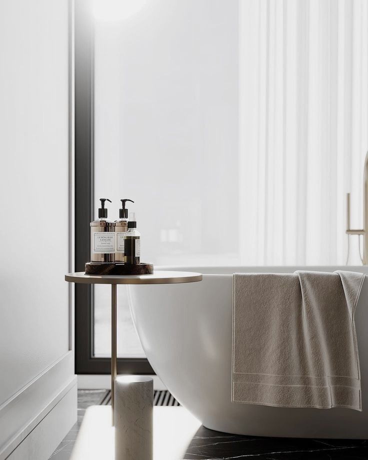 A serene modern bathroom scene with a white freestanding bathtub, a light beige towel draped over its edge, and an elegant side table holding toiletries, illuminated by soft light from a window with sheer curtains.