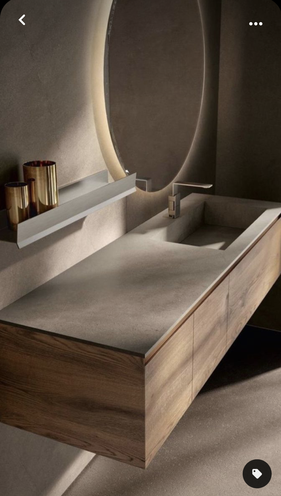 A modern minimalist bathroom featuring a floating wood vanity with a grey stone-look integrated sink, a large backlit oval mirror, and warm ambient lighting creating a sophisticated, moody atmosphere.