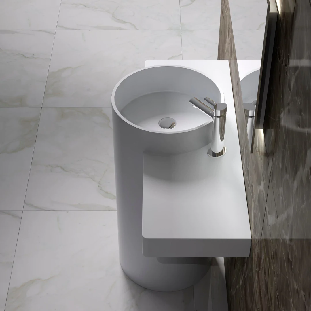 Ultra-modern minimalist bathroom with a white cylindrical pedestal sink featuring an integrated side shelf, a chrome faucet, white marble-effect tiled flooring, and a contrasting dark marble wall with a large mirror.