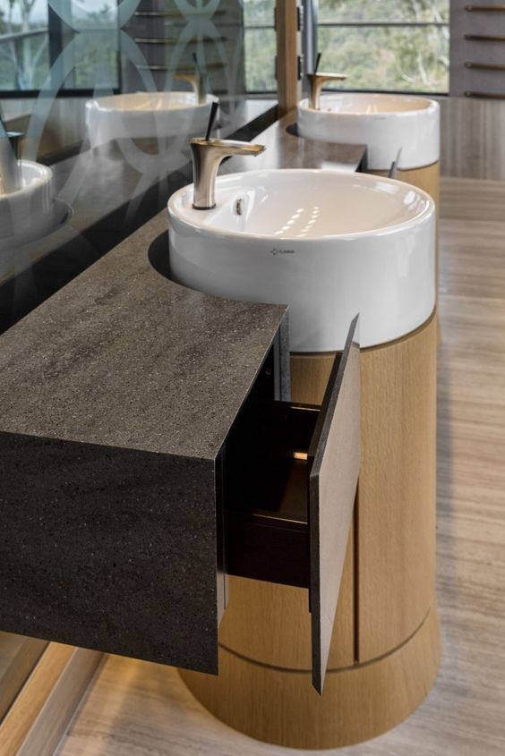 Sleek contemporary bathroom featuring a white vessel sink on a light wood cylindrical pedestal, complemented by a dark textured minimalist floating drawer unit.