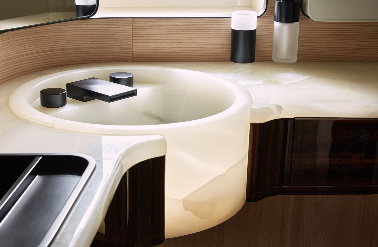 Ultra-luxurious bathroom featuring a stunning circular backlit onyx washbasin with seamlessly integrated dark modern faucets, glowing warmly on a matching countertop, adjacent to rich dark wood cabinetry.