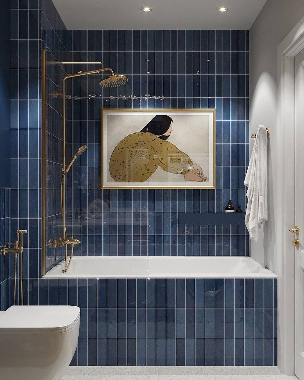 Built-in bathtub in a modern bathroom featuring deep blue vertical subway tiles, gold shower fixtures, and artwork hanging on the wall above the tub.