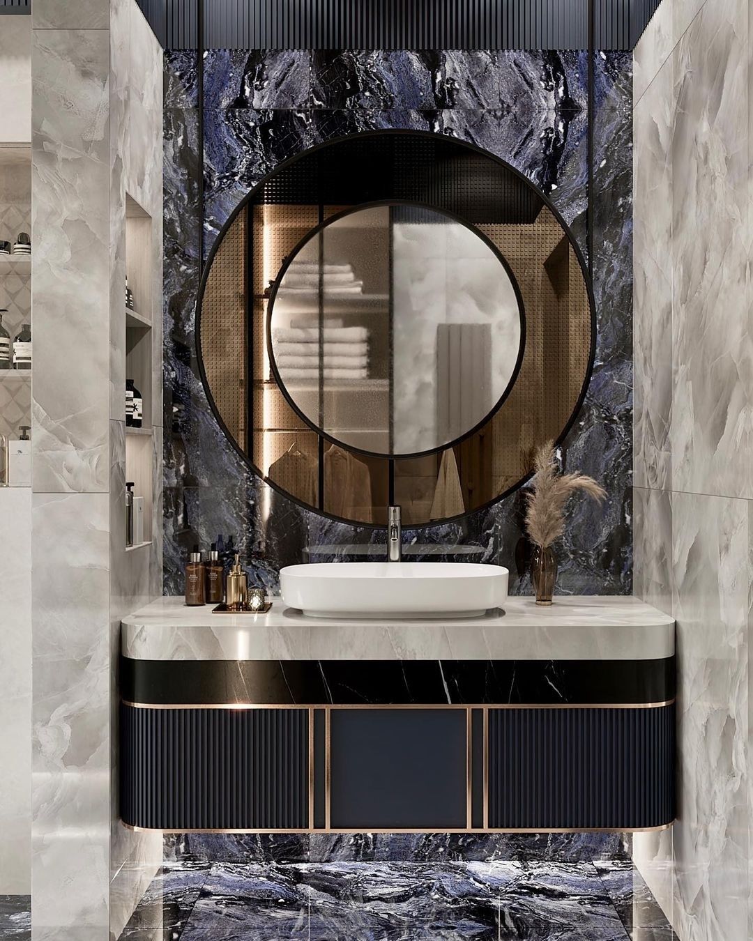 A modern luxury bathroom vanity area featuring a dark blue ribbed vanity with a white marble countertop and an oval vessel sink, against a dark blue marble back wall adorned with a circular mirror with a gold decorative ring.