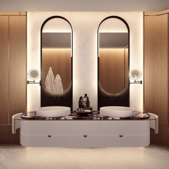 A modern luxury bathroom features a light pink ribbed double vanity, a purple-patterned stone countertop, two white round vessel sinks, and arch-shaped black-framed mirrors with LED backlighting.