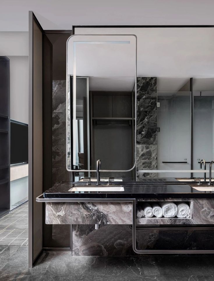 Modern luxury hotel bathroom featuring a black marble countertop vanity, undermount sink, and a large illuminated mirror.