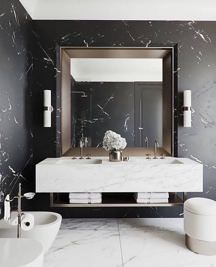 Modern luxury bathroom featuring a white marble floating vanity, a large mirror with a bronze metal frame, and a black marble accent wall.