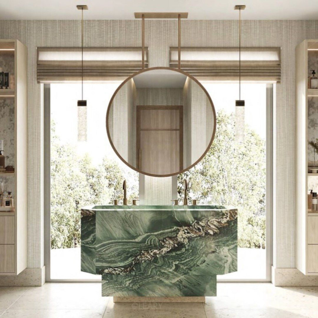 A modern luxury bathroom by architect Charles Zana, featuring a freestanding green marble sink with a large circular mirror suspended from the ceiling in front of a floor-to-ceiling window.