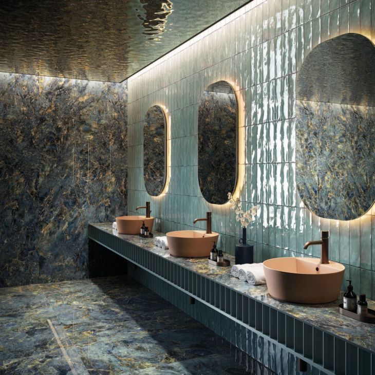 A luxury bathroom featuring three matte terracotta vessel sinks on a dark green fluted vanity, with capsule-shaped backlit mirrors and dramatic blue and green stone walls.