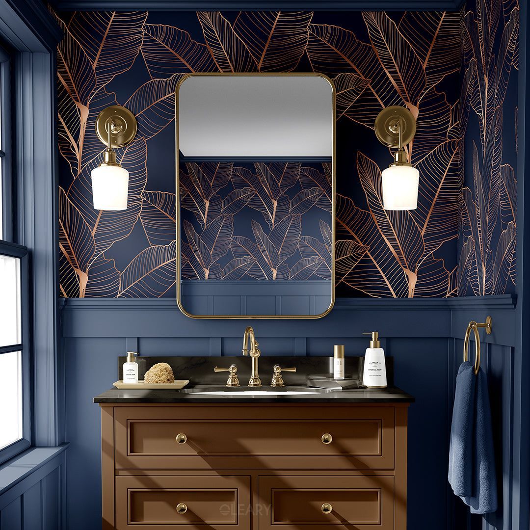 An elegant bathroom with navy blue walls and botanical wallpaper, featuring a classic brown wood vanity with a dark countertop, a white undermount sink, and brushed gold fixtures.
