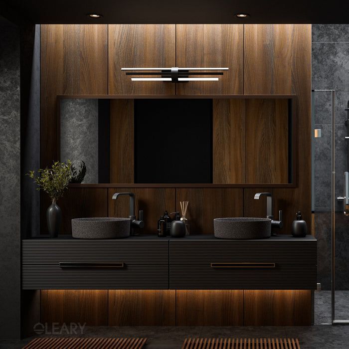 A moody, modern bathroom featuring a dark floating vanity with ribbed drawers, stone vessel sinks, and a warm wood accent wall illuminated by a sculptural light and under-cabinet glow.