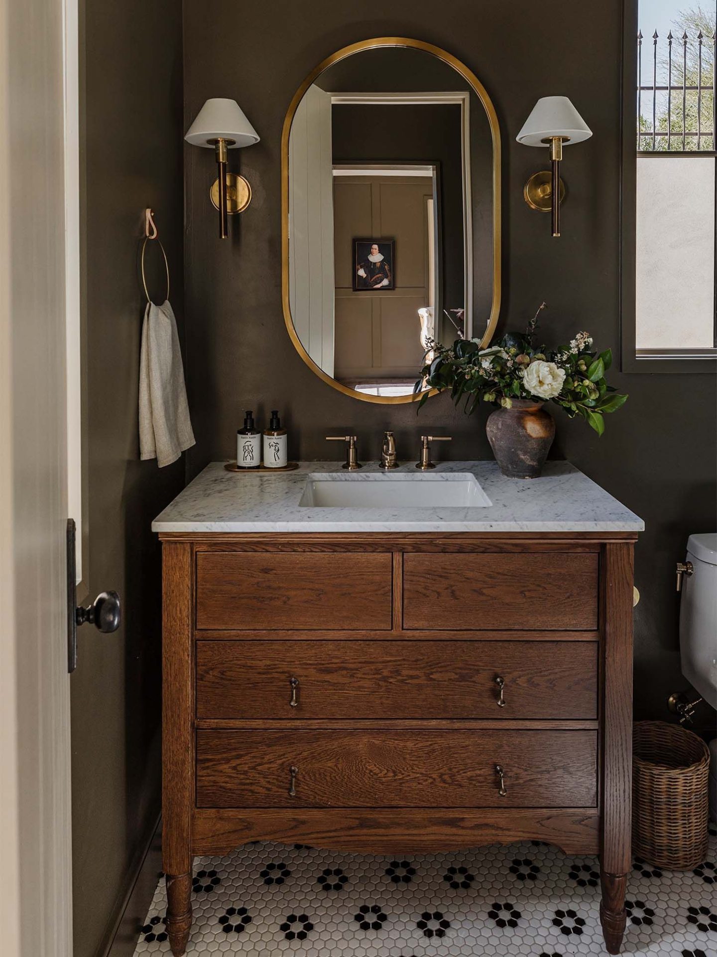 Vintage-style bathroom with solid wood vanity, marble countertop, hexagonal floral floor tiles, and gold-framed mirror with wall sconces.

