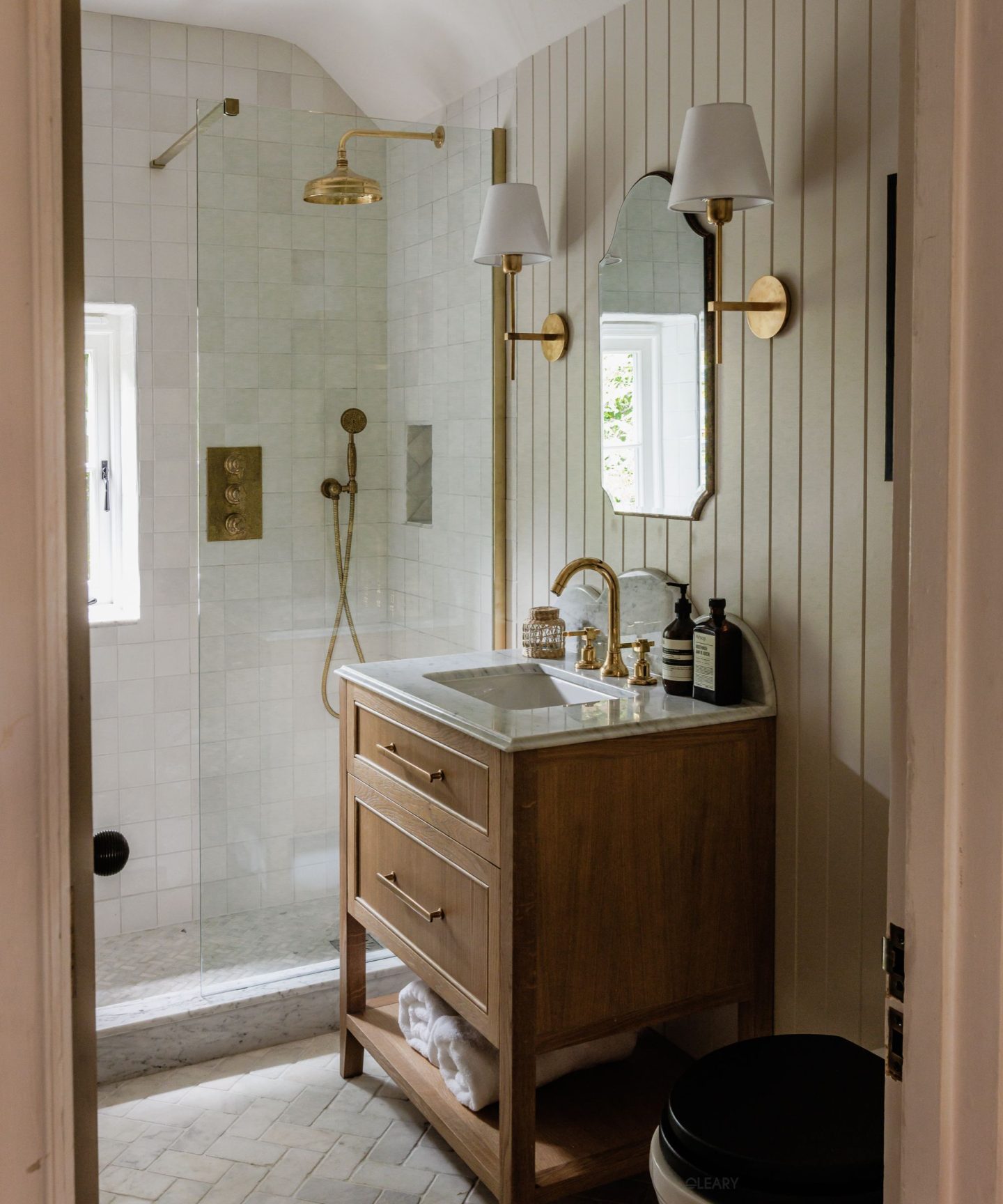 A small bathroom with a solid wood vanity, under-mount sink, brass fixtures, and glass-enclosed shower—styled with natural elegance.

