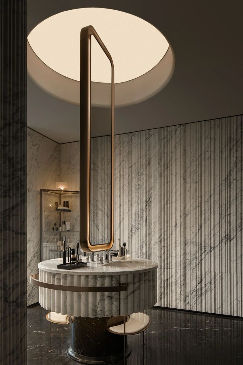Luxurious modern bathroom featuring a round freestanding marble vanity with fluted texture, topped by an elongated oval mirror and circular ceiling light.