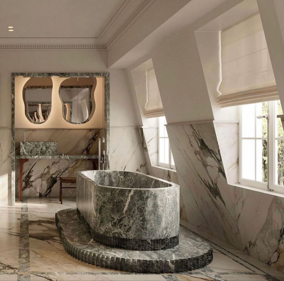 A grand attic bathroom featuring a large, freestanding green marble bathtub on a custom fluted marble pedestal. The walls and floor are clad in matching veined marble, with a vanity area featuring abstract mirrors, under-sink lighting, and two large windows with Roman blinds.