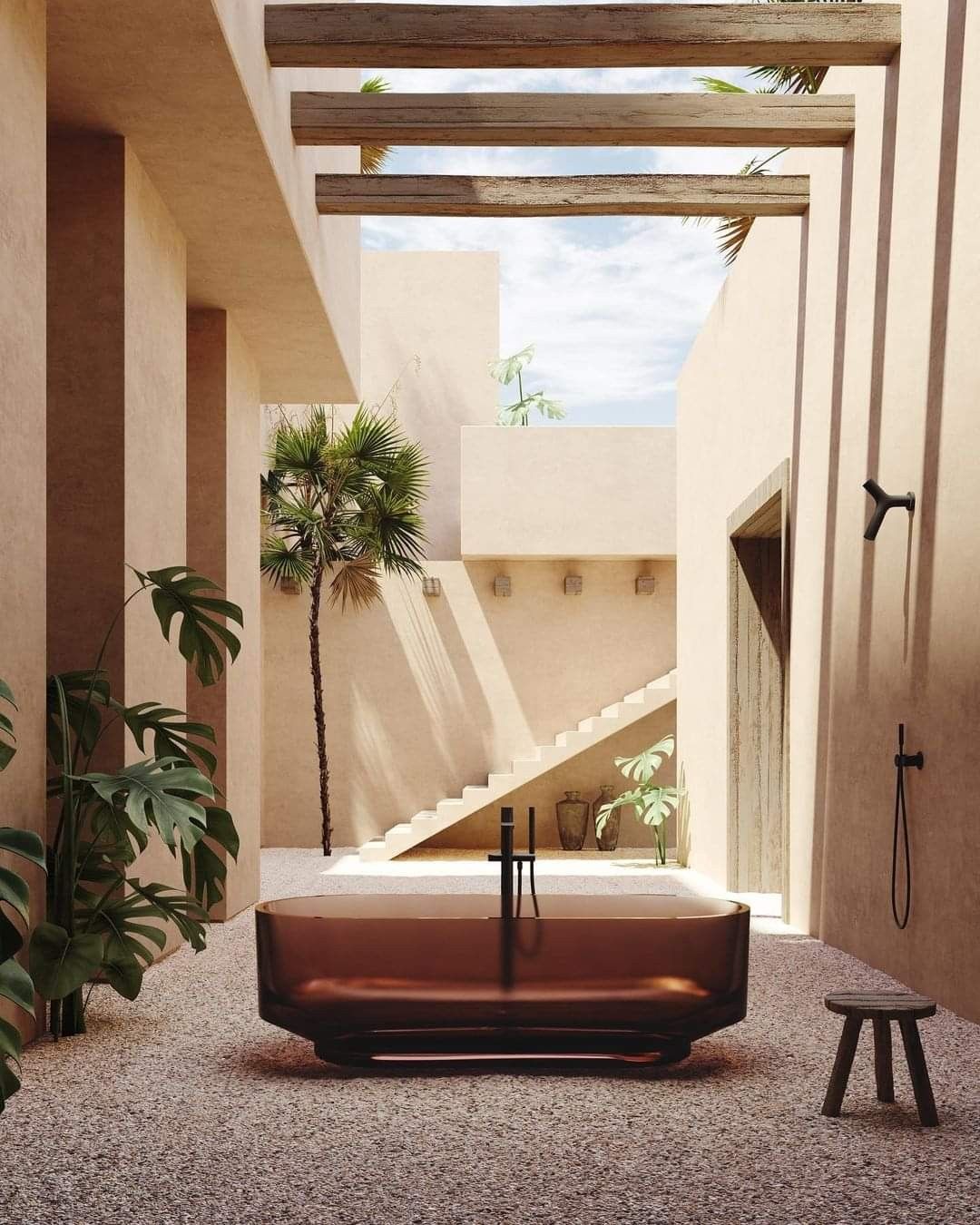 Deep brown transparent resin bathtub in an outdoor courtyard, surrounded by tropical plants and sand-colored architecture, creating a luxurious and private ambiance.