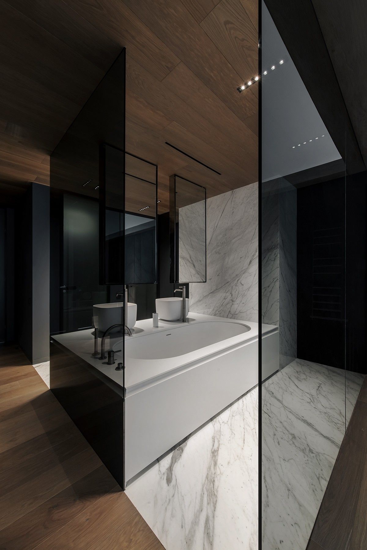 White recessed oval bathtub clad in white marble, paired with double basins, in a modern luxury bathroom.