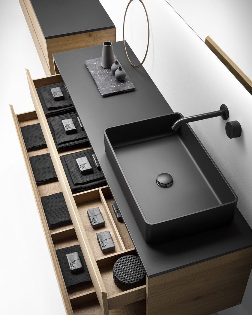 Modern minimalist bathroom vanity featuring a light wood floating cabinet with open, compartmentalized drawers, a black square vessel sink, and a matte black wall-mounted faucet, on a dark countertop.