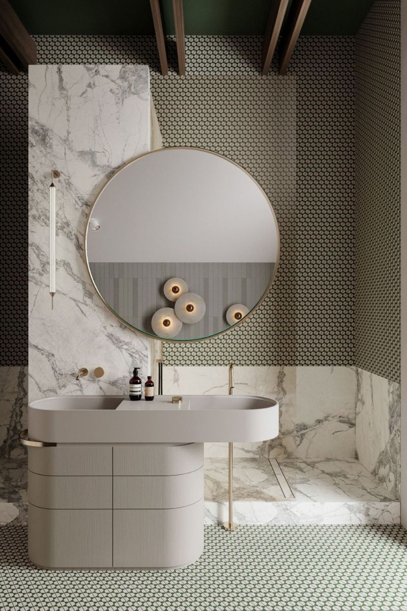 Artistic modern bathroom featuring a unique light grey curved freestanding bathroom cabinet with an integrated elongated oval washbasin, wall-mounted gold faucets, a large round mirror with distinctive lighting, and contrasting marble and mosaic tile walls.