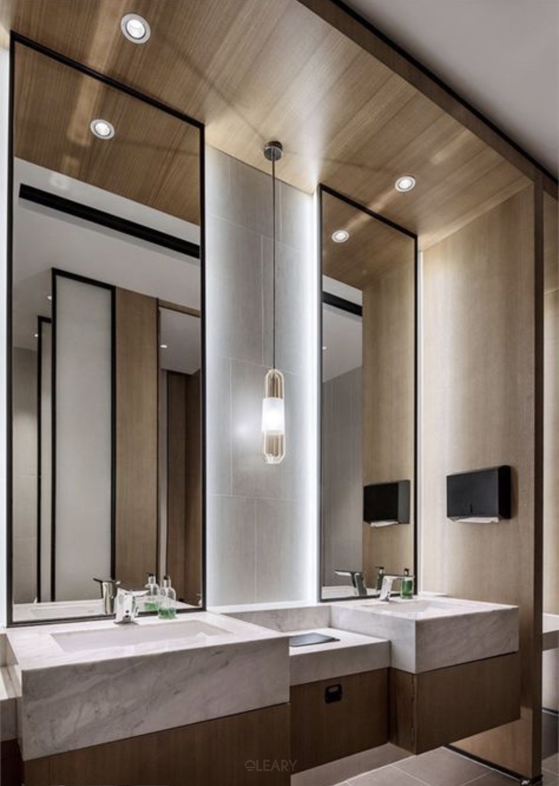A luxury commercial restroom designed with Axon commercial under-mount sinks set in a custom marble and wood vanity, complemented by tall Axon black-framed rectangular mirrors and elegant lighting.