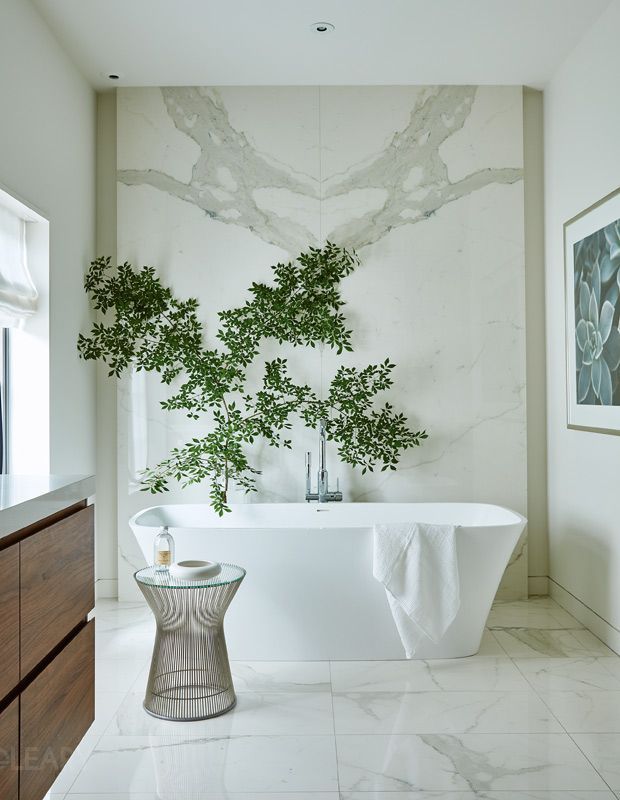 The Serene Collection showcased in a minimalist bathroom, featuring the modern floating wood vanity and the white, oval freestanding bathtub set against a book-matched white marble wall with an artistic green branch accent.