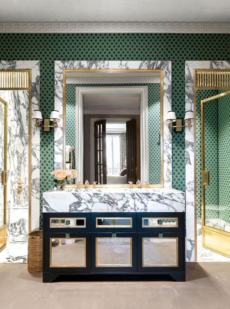The Regency Grand Neoclassical vanity cabinet, shown in a deep blue high-gloss lacquer with mirrored and solid brass-trimmed doors, featuring a substantial Calacatta marble top and backsplash. It is set in a modern luxury bathroom with bold green geometric wallpaper.