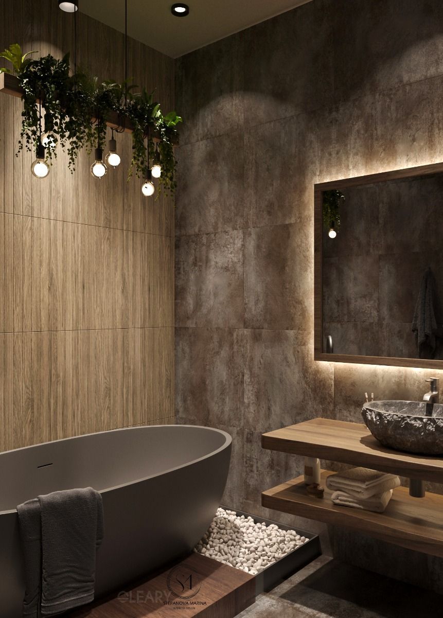 An industrial-style bathroom featuring a rough, natural stone vessel sink on a rustic wood vanity, a matte grey freestanding tub, and a custom light fixture with plants and Edison bulbs.