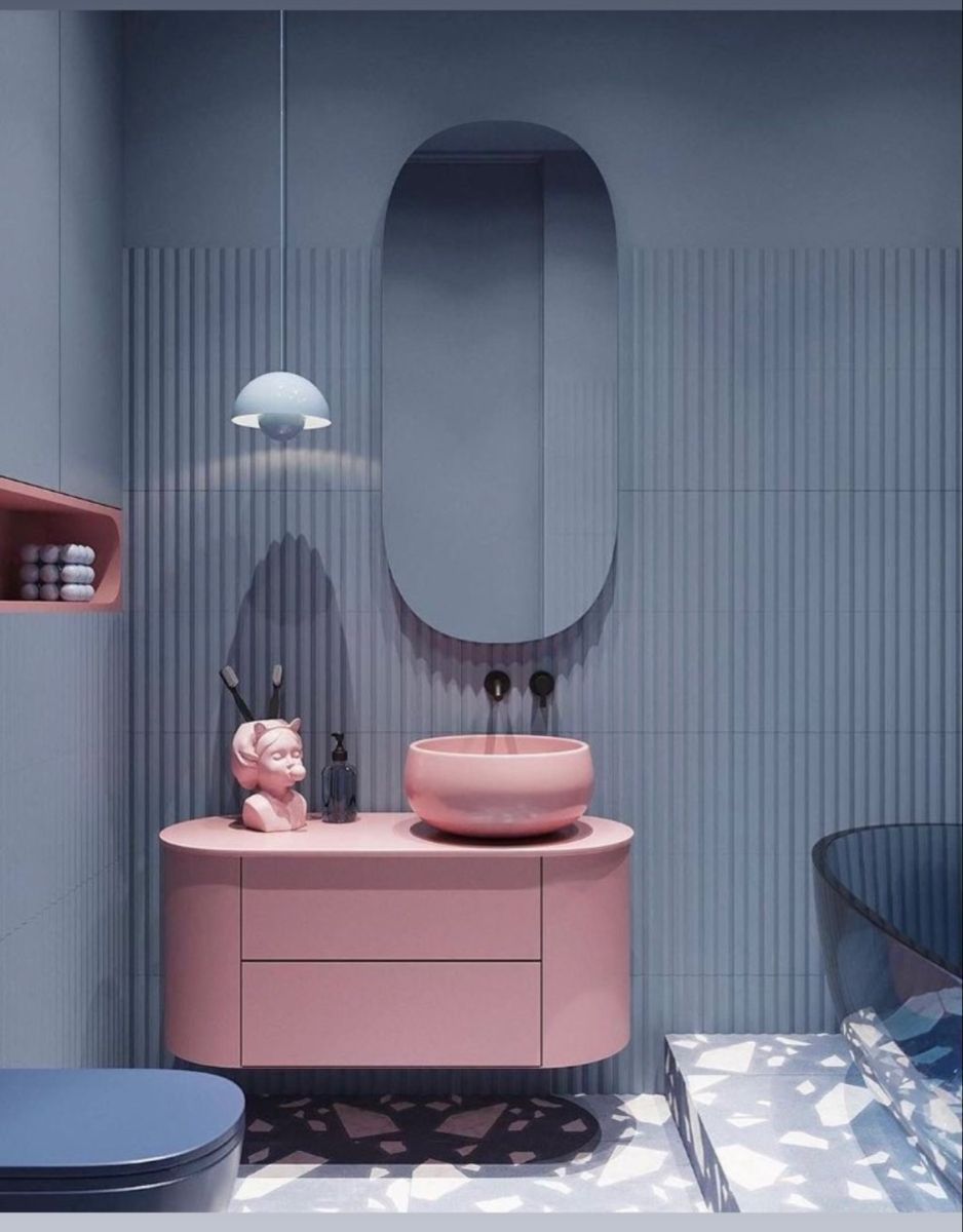 A modern, color-blocked bathroom featuring a pink floating vanity and matching pink vessel sink against a blue fluted tile wall with a terrazzo floor.