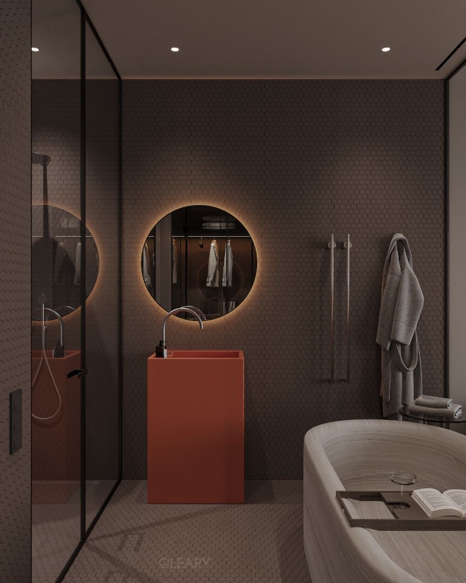 A modern dark bathroom featuring a bold, burnt orange freestanding pedestal sink as a focal point, illuminated by a round backlit LED mirror against dark hexagonal tile walls.