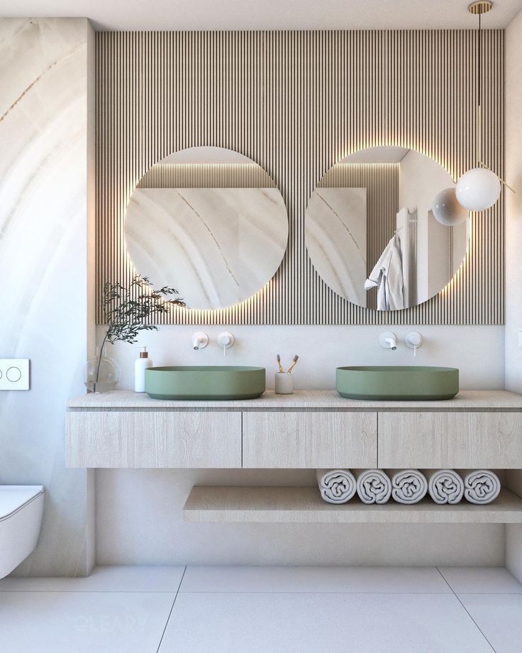 A serene Japandi-style bathroom with a light oak floating double vanity, two sage green vessel sinks, and two round backlit LED mirrors against a fluted wood accent wall.