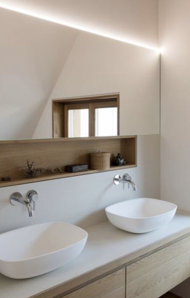A serene Japandi-style bathroom with a light oak double vanity, two white asymmetrical vessel sinks, and a wall-to-wall mirror with overhead integrated LED lighting.