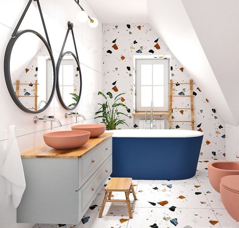 A playful and colorful attic bathroom featuring a bold blue freestanding tub, two terracotta vessel sinks, and multi-color terrazzo on the walls and floor.