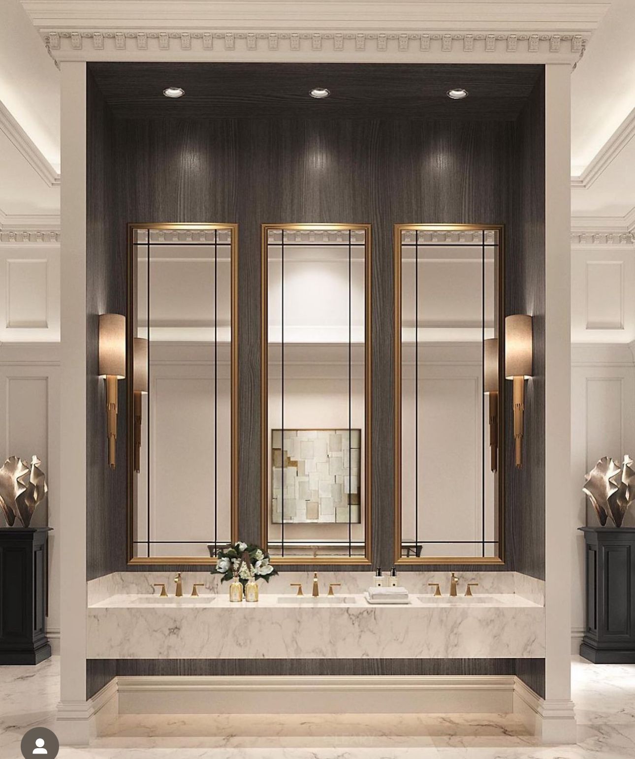 A luxurious Art Deco style bathroom featuring a long white marble vanity with three integrated sinks, and three tall, gold-framed geometric mirrors set against a dark wood accent wall.