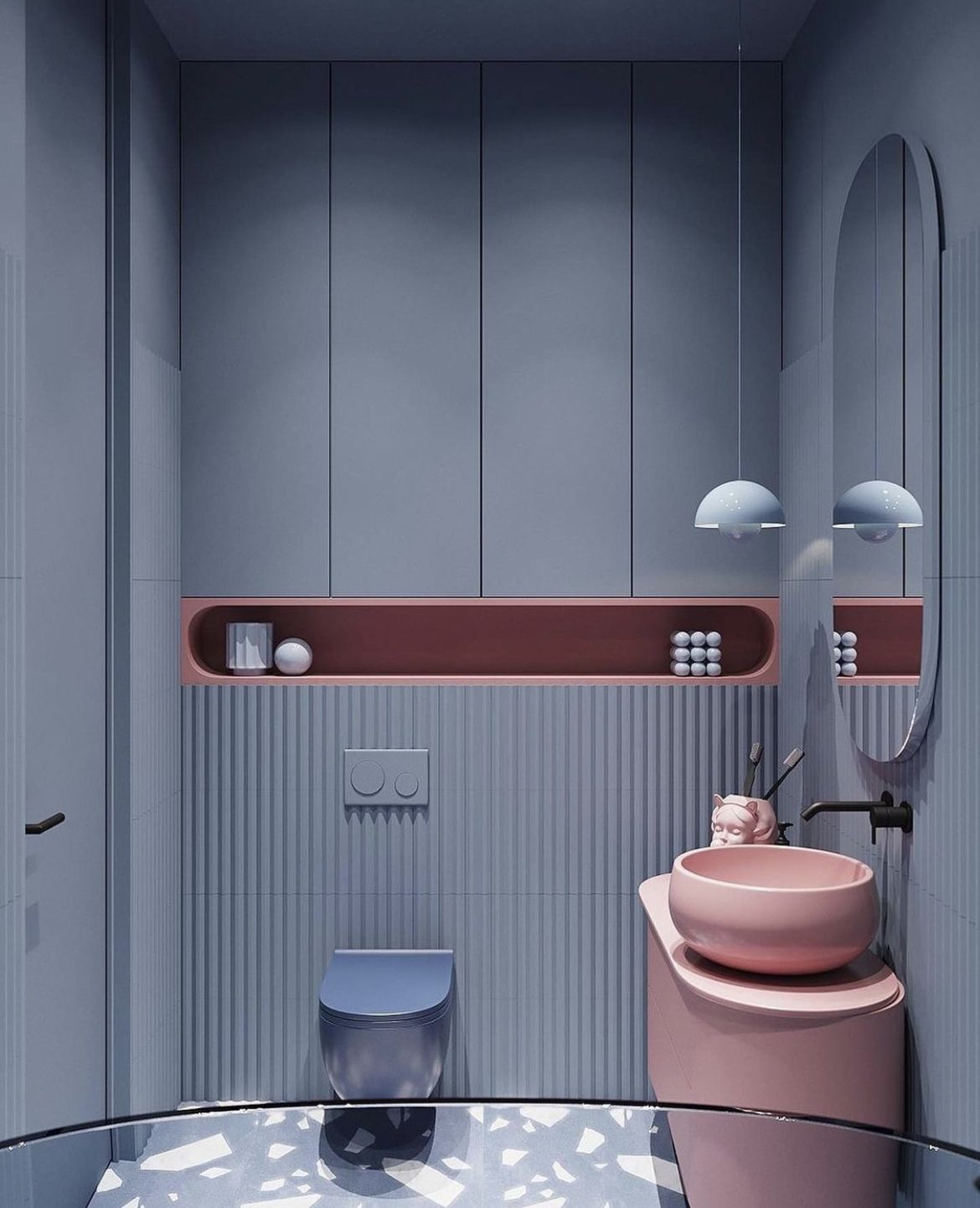 Bold modern bathroom featuring a pink freestanding pedestal sink, a pink wall-mounted toilet, and blue-grey vertical fluted wall tiles, with an oval mirror and white pendant lights.