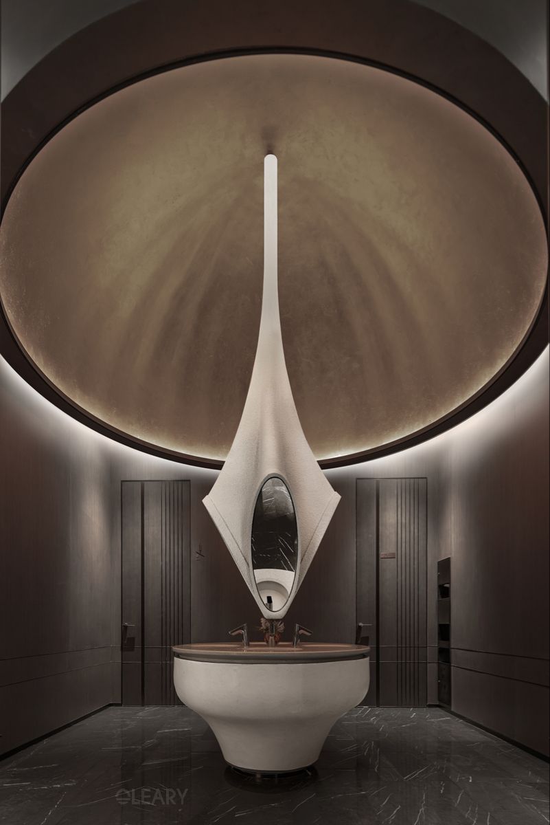 Ultra-futuristic luxury bathroom featuring a white sculptural integrated vanity and eye-shaped mirror suspended from a luminous brass-toned circular dome ceiling, with dark textured walls.
