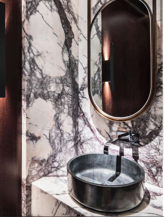 Dark metal countertop basin with a brushed finish, paired with a wall-mounted faucet and an oval mirror, set in a luxurious marble bathroom.