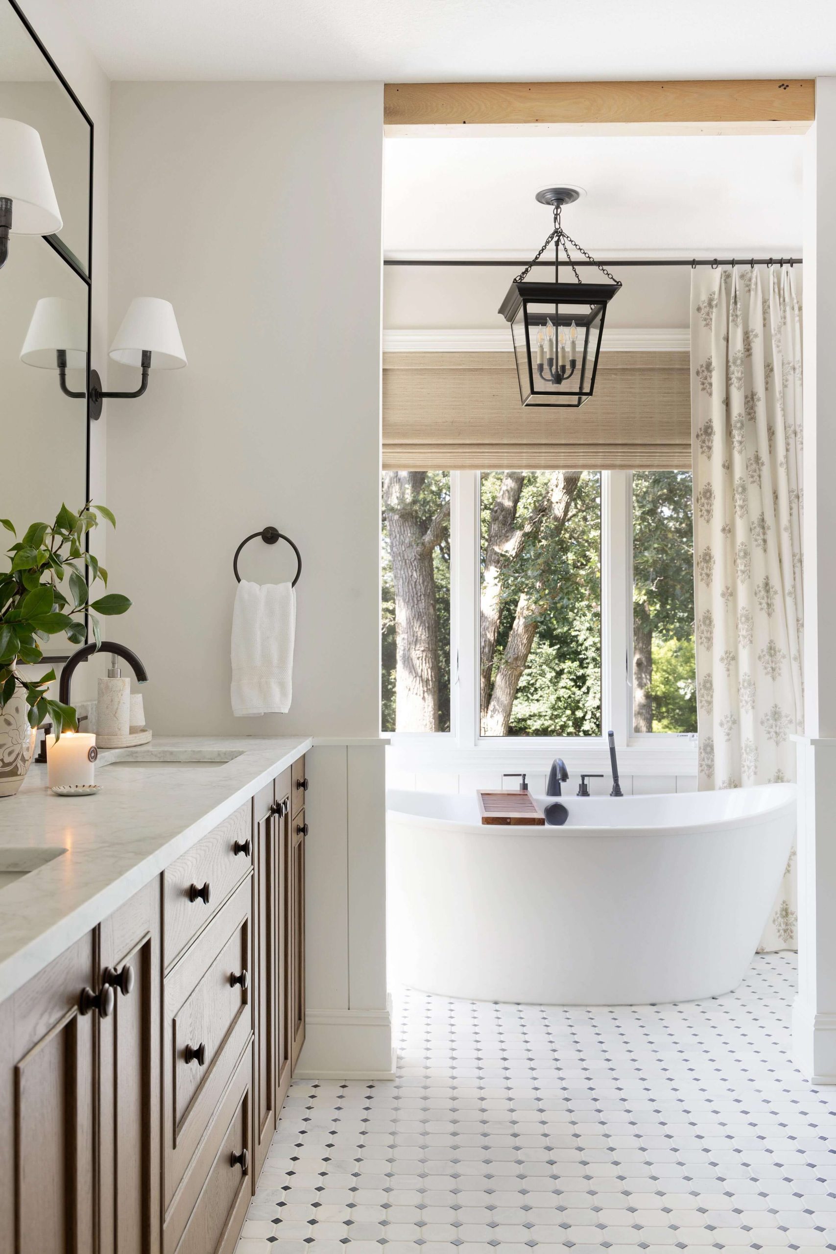 Bright, classic-style bathroom with a white freestanding bathtub by a large window, dark wood vanity, white mosaic floor, and a black lantern pendant light.