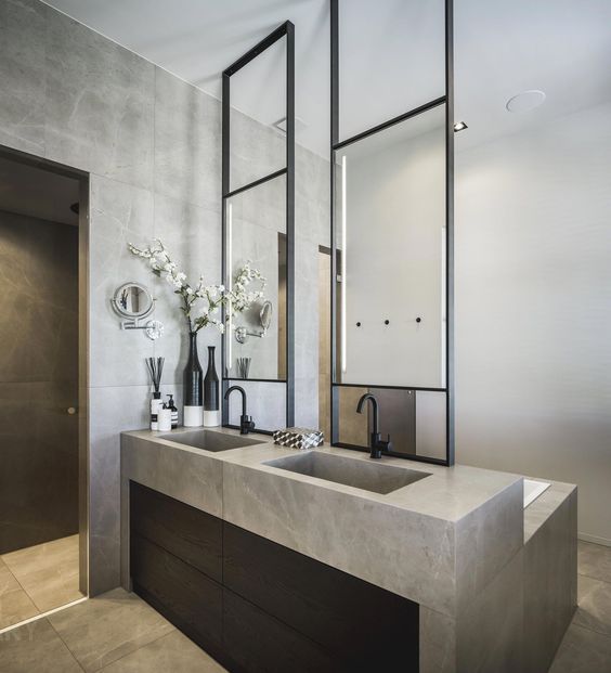 Modern industrial bathroom with a custom double stone vanity and integrated sinks, topped by black metal-framed floating mirrors with integrated lighting.