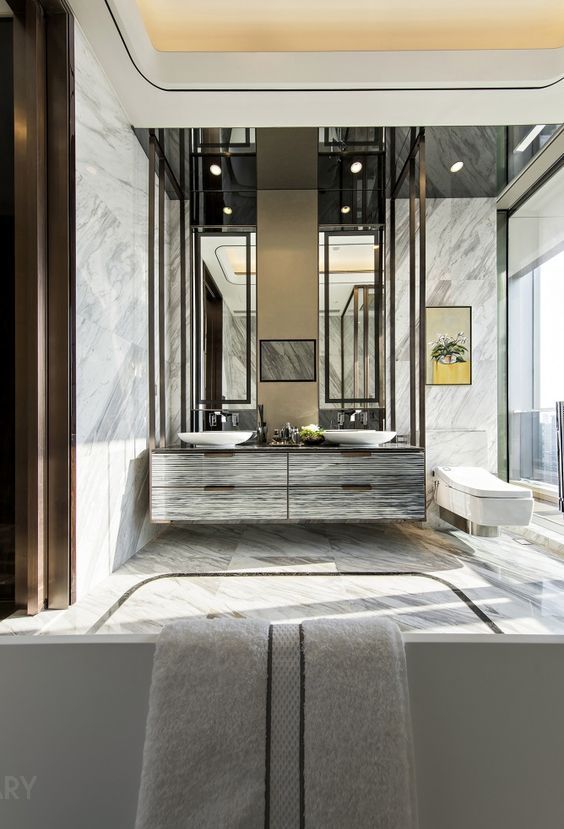 Custom double white marble vanity with integrated sinks, topped by black metal-framed artistic mirrors with integrated lighting, in a luxurious hotel bathroom.