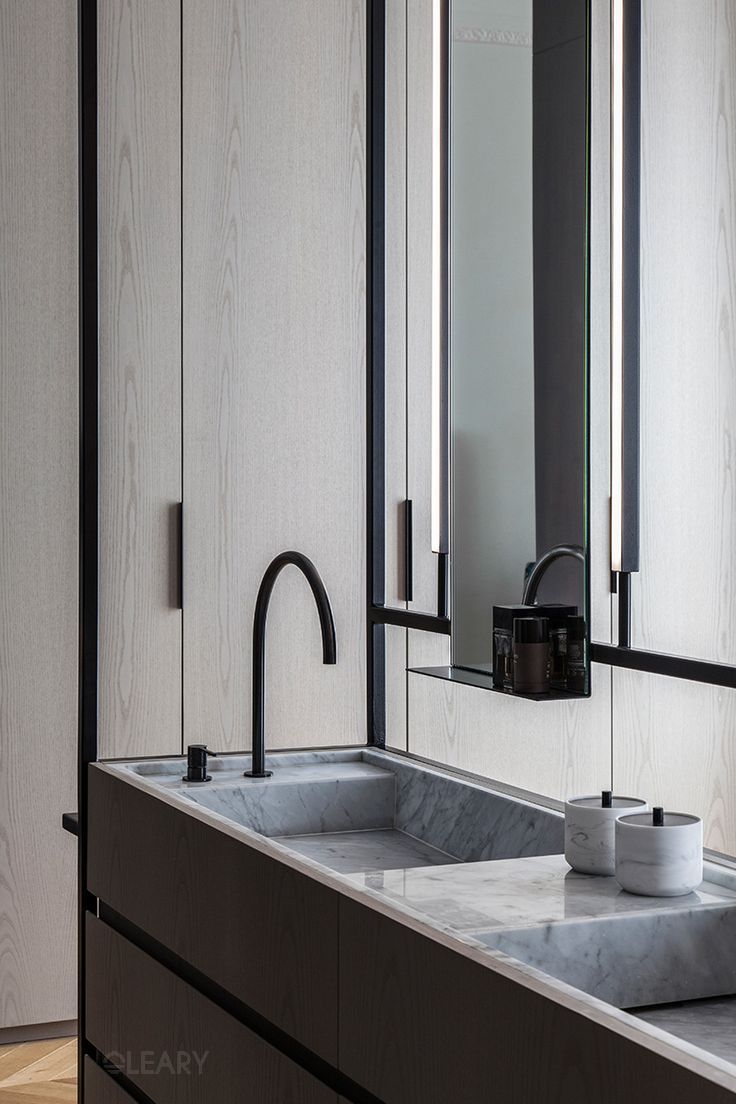 Modern bathroom featuring an integrated marble sink vanity, a matte black faucet, and light wood cabinetry with a sleek mirror and vertical LED lighting.