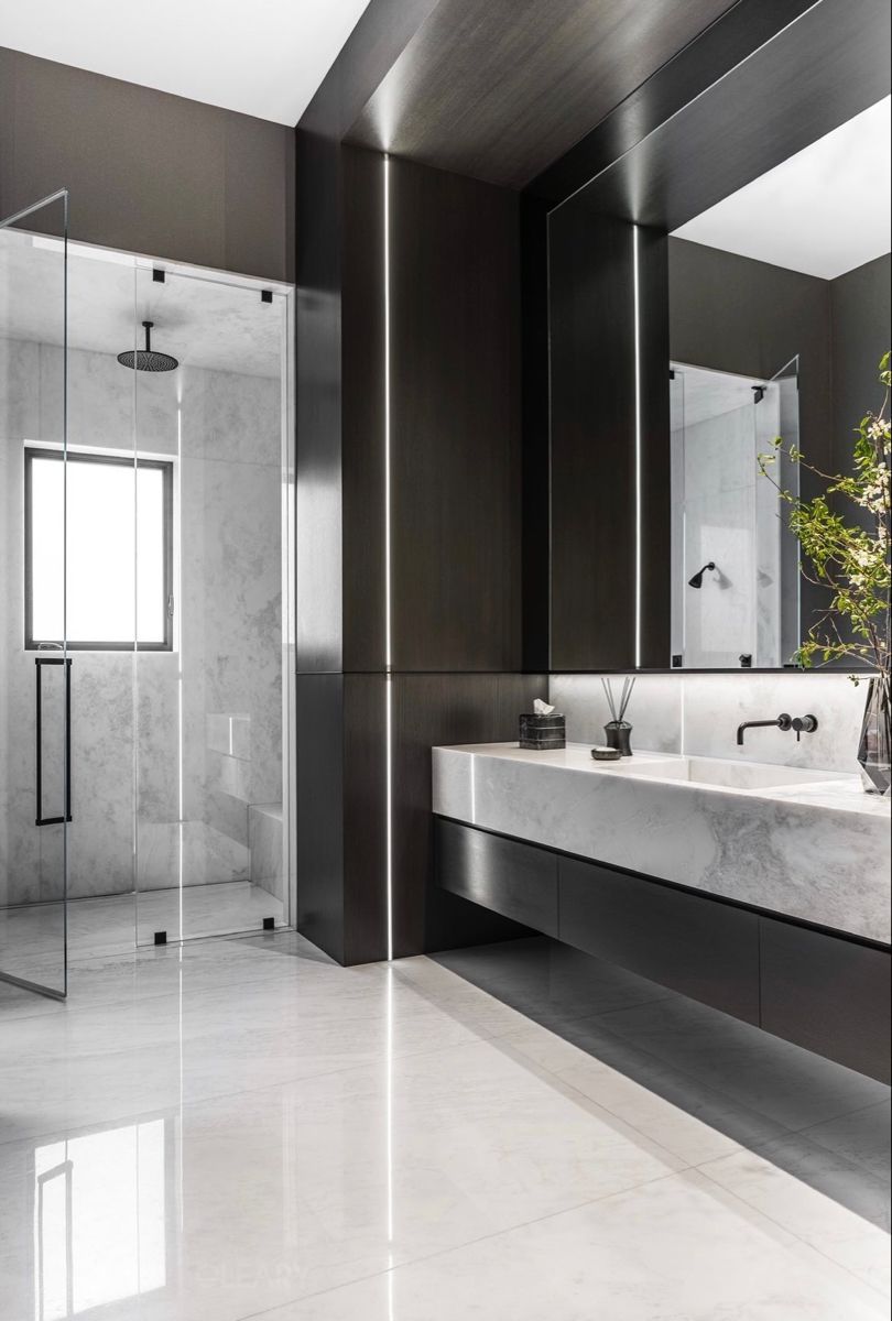 Luxury modern bathroom with a floating white marble double vanity, integrated sinks, matte black wall-mounted faucets, and dramatic vertical LED strip lighting on dark walls.