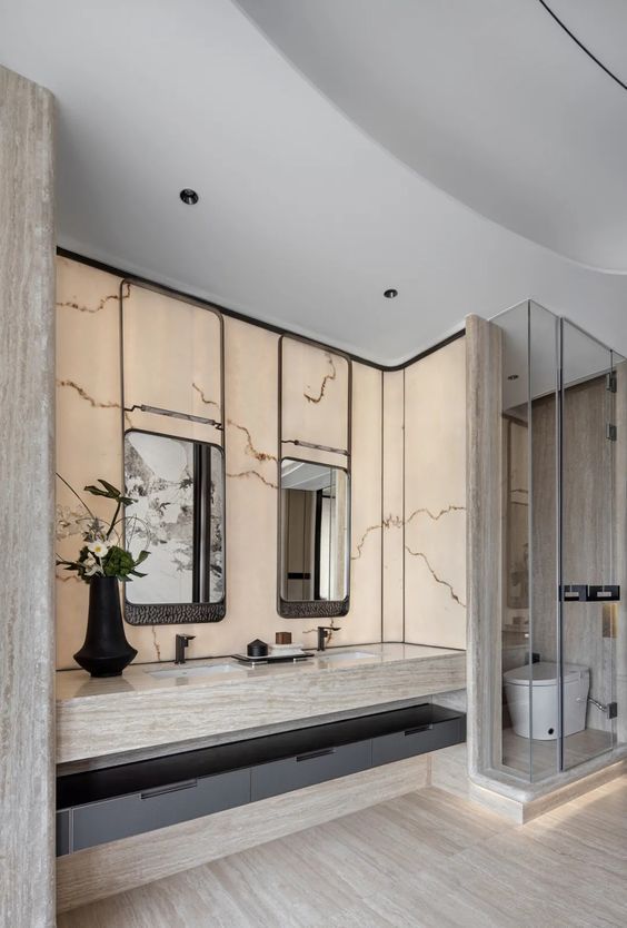 Luxurious hotel bathroom featuring a double natural stone vanity with integrated sinks, a backlit onyx wall, and unique framed mirrors.