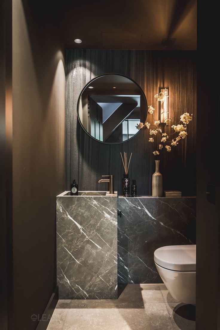 Luxury compact powder room with a monolithic dark marble vanity and integrated sink, round mirror, matte black faucet, and elegant wall sconces.