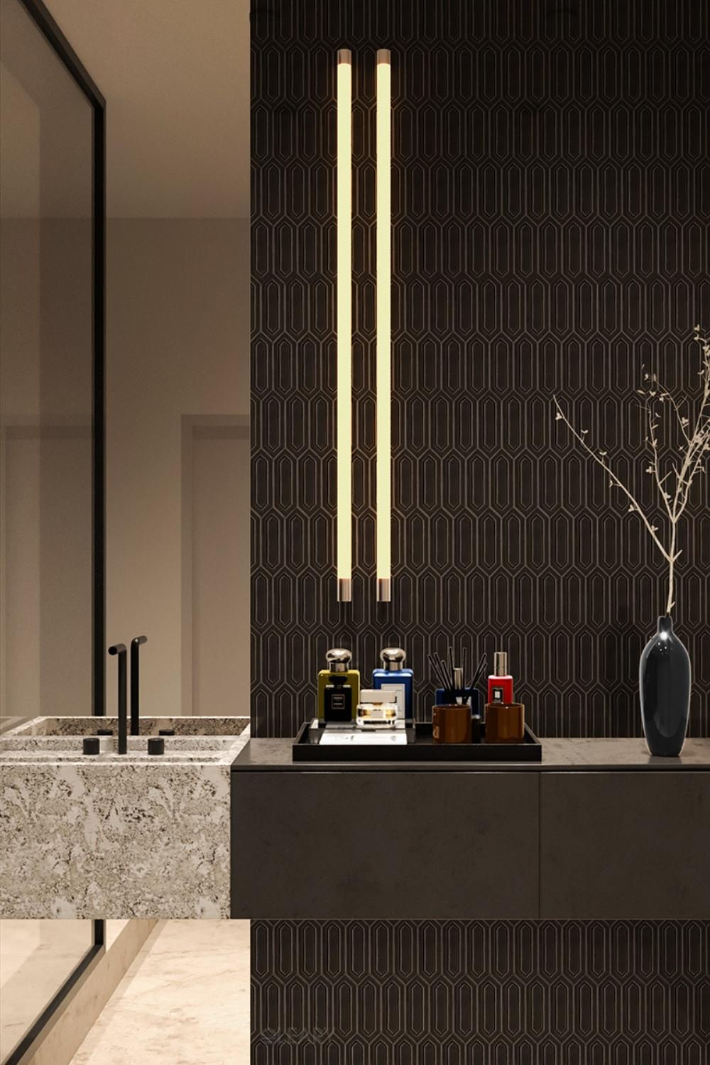 Luxury modern bathroom with a unique speckled sink, black floating vanity, dark geometric patterned wall tiles, wall-mounted matte black faucets, and vertical linear pendant lights.