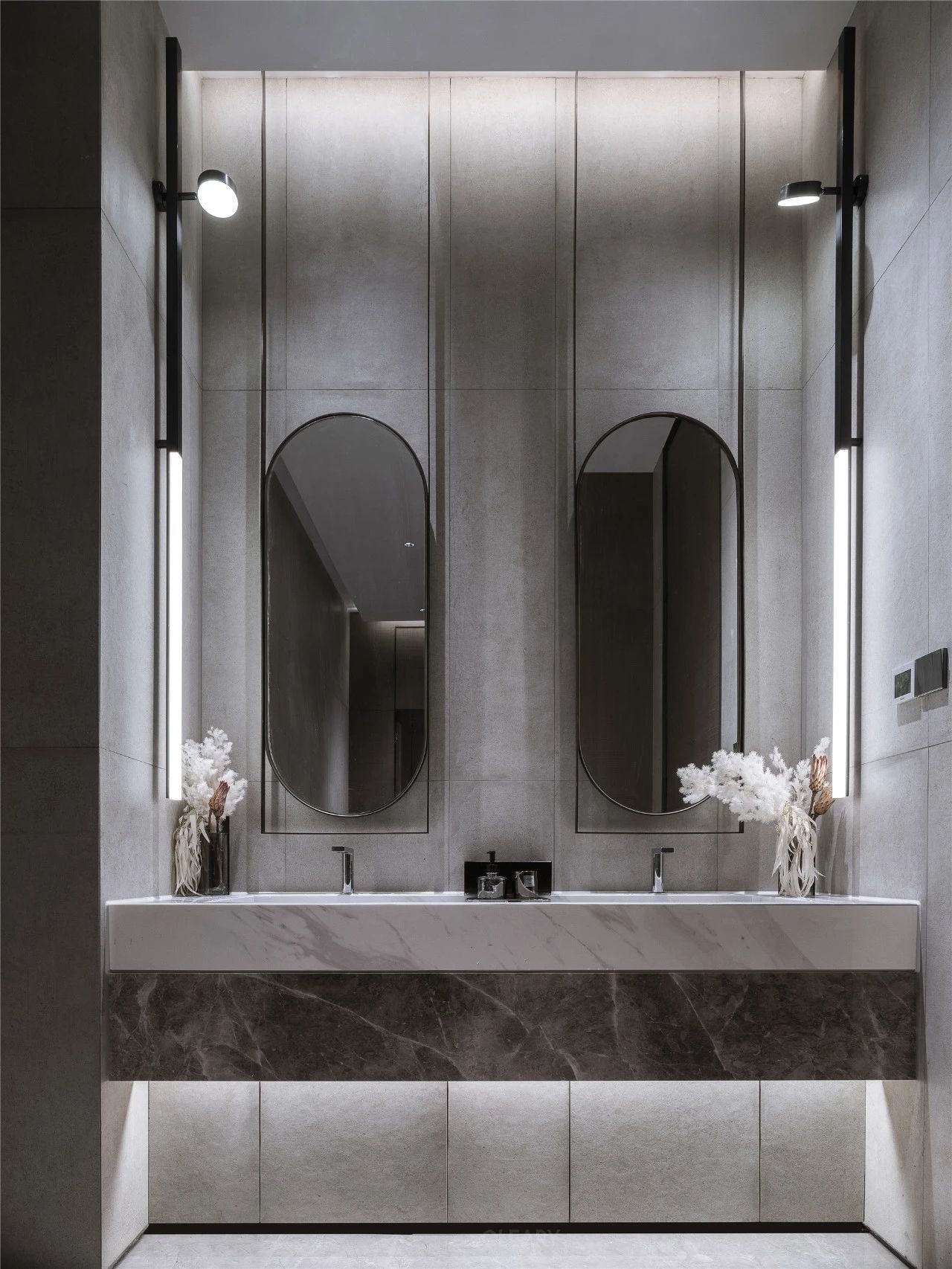 A sophisticated modern double vanity with a layered white and dark marble countertop, dual undermount sinks, and vertical LED wall sconces in a grey tiled bathroom.