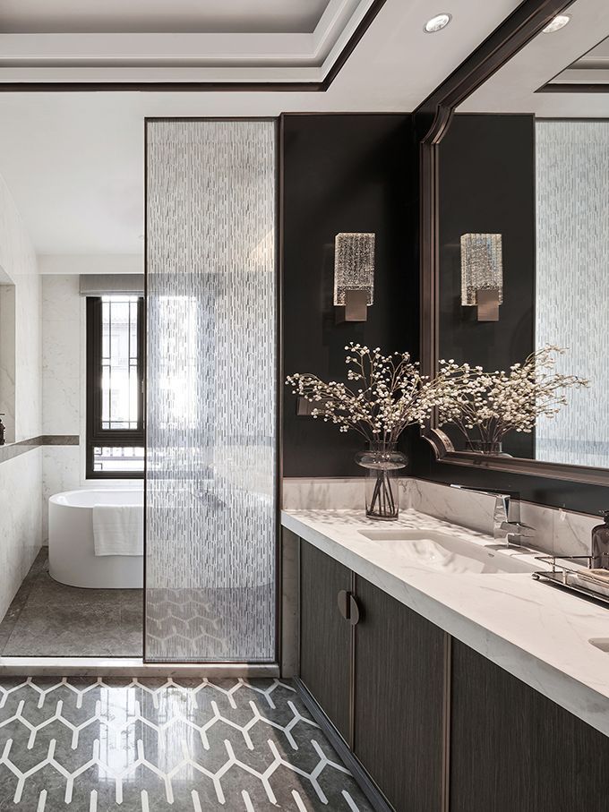 Modern luxury bathroom vanity with white countertop, dark wood cabinets, large mirror, and elegant wall sconces, separated by a frosted glass partition.