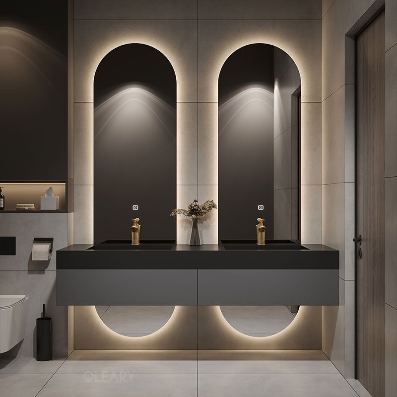 Modern luxury bathroom with a black floating double vanity, integrated white sinks, gold faucets, arched backlit mirrors, and light grey tiled walls.