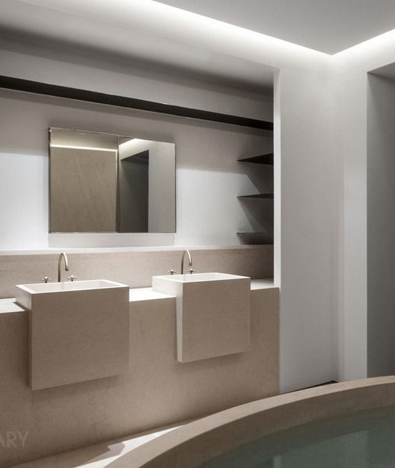 Two square white wall-mounted basins with gold faucets and concealed lighting in a modern minimalist bathroom.