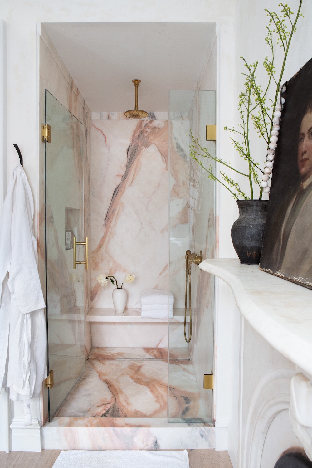 An ultra-luxurious walk-in shower with pink-toned marble cladding, featuring gold shower fixtures, glass doors, and an integrated bench.